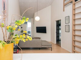 Un soggiorno moderno con un divano grigio, una televisione a schermo piatto fissata al muro e una libreria a scala in legno.