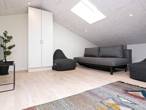 A modern loft bedroom with a sloped ceiling, a built-in wardrobe, a sofa bed, a small seating area, and a colorful rug. - 5 Star Holiday Home in Ringkobing (Ringkobing)