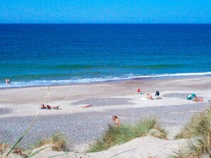 A beach with people sunbathing and swimming, and dunes in the foreground. - 5 Star Holiday Home in Ringkobing (Ringkobing)