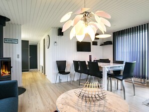 A modern living room with a fireplace, a dining area with chairs, a table, and a unique ceiling light fixture. - 4 Star Holiday Home in Vinderup (Vinderup)