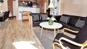 A modern living room with a black leather sofa, a round coffee table, and a dining area with a white table and chairs. - 7 Person Holiday Home in Hemmet (Hemmet)
