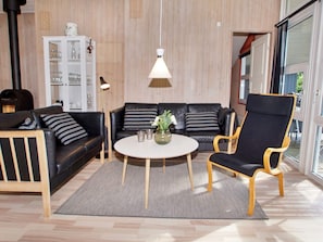 Un salon comprenant un canapé, un fauteuil et une table ronde, un parquet et un meuble contenant de la verrerie.