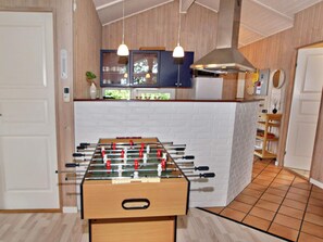 A room with a foosball table, wooden cabinets, a white brick wall, and pendant lighting.
