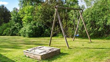 A wooden swing set in a grassy area with dense foliage in the background.