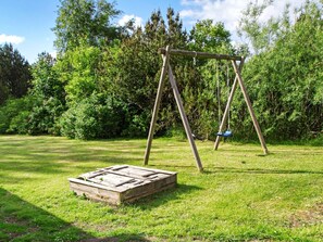 A wooden swing set in a grassy area with dense foliage in the background.