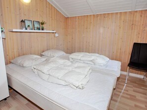 A bedroom with a wooden wall, a bed with white bedding, a chair, and a shelf with decorative items. - 7 Person Holiday Home in Hemmet (Hemmet)