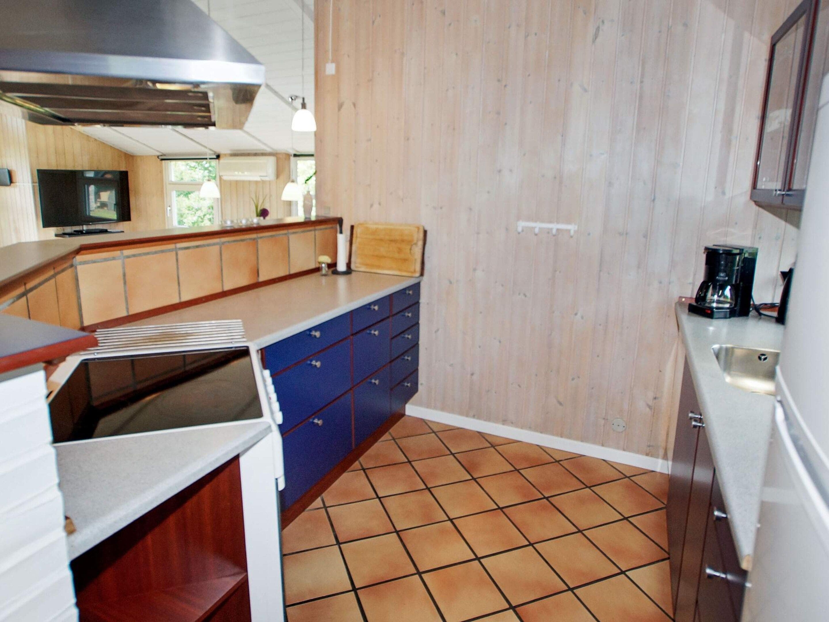 Una cocina con suelo de baldosas, armarios de madera, horno empotrado y cafetera sobre la encimera.