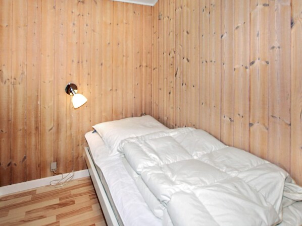 A single bed in a room with wooden panel walls and a wooden floor.