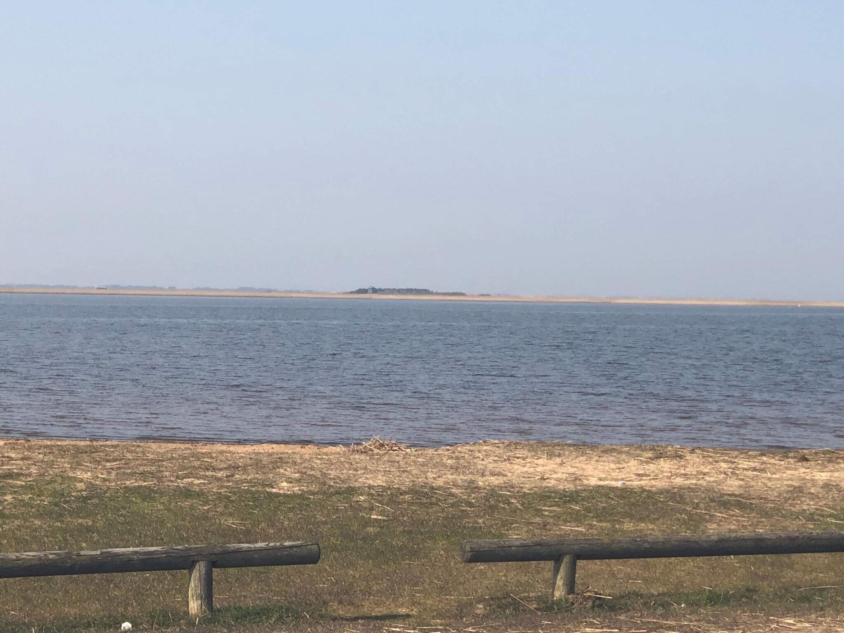 Uitzicht op een strand, met een houten hek op de voorgrond en een eiland in de verte.