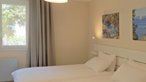A bedroom with a bed, a window with curtains, and two wall-mounted paintings. - Front de mer / 3 Pièces 91 m2 / 3ème Avec Ascenseur / Parking / 4 (Bandol)