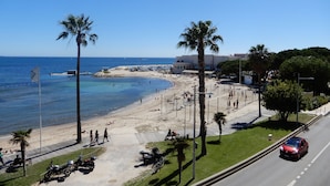 A beach with palm trees, a road, and a clear blue sky. - Front de mer / 3 Pièces 91 m2 / 3ème Avec Ascenseur / Parking / 4 (Bandol)
