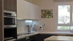A modern kitchen with built-in appliances, a dining area with a table and chairs, and a window providing natural light. - Front de mer / 3 Pièces 91 m2 / 3ème Avec Ascenseur / Parking / 4 (Bandol)