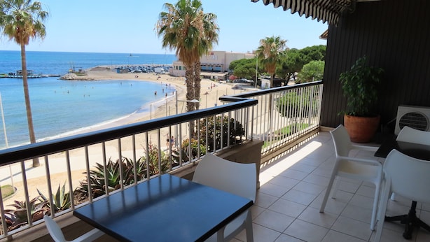 A balcony with a view of the beach, white chairs, a table, and a potted plant. - Front de mer / 3 Pièces 91 m2 / 3ème Avec Ascenseur / Parking / 4 (Bandol)