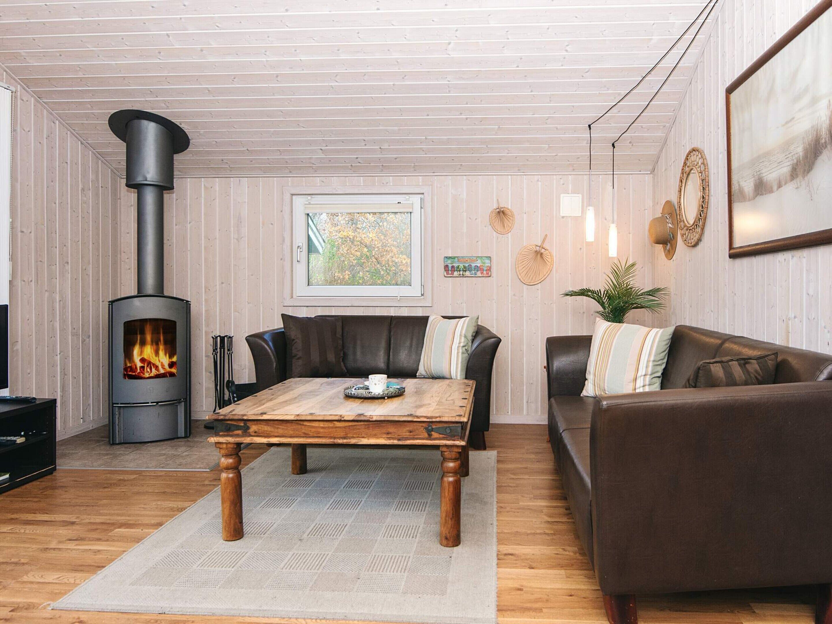Een gezellige woonkamer met een houtkachel, leren banken, een houten salontafel en uitzicht op de natuur door een raam.