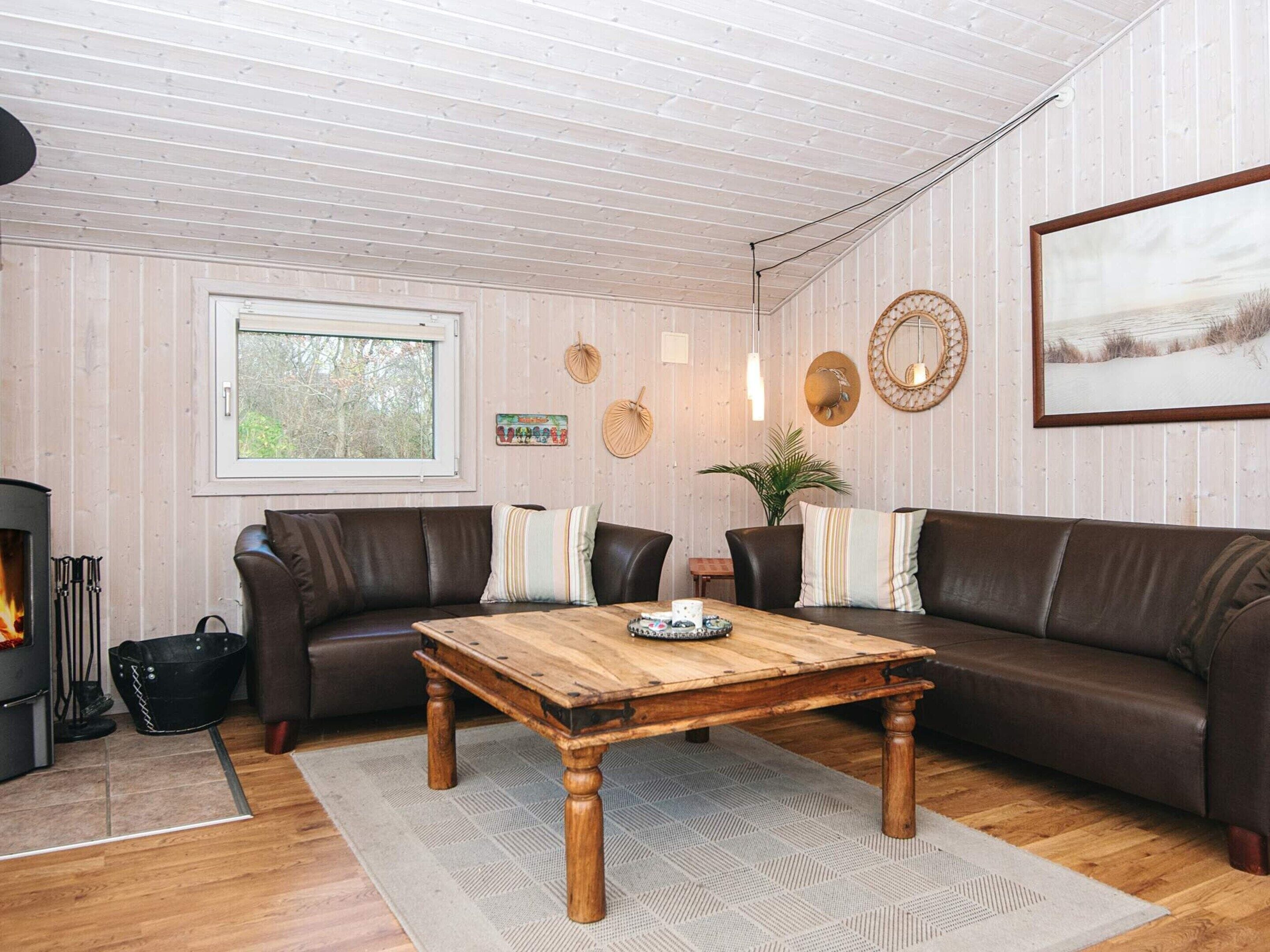 A cozy living room with a fireplace, leather sofas, a wooden coffee table, and a large window.