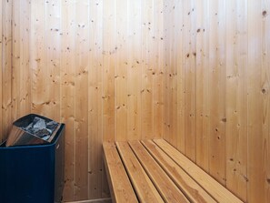 A sauna with wooden walls, a bench, and a trash bin.