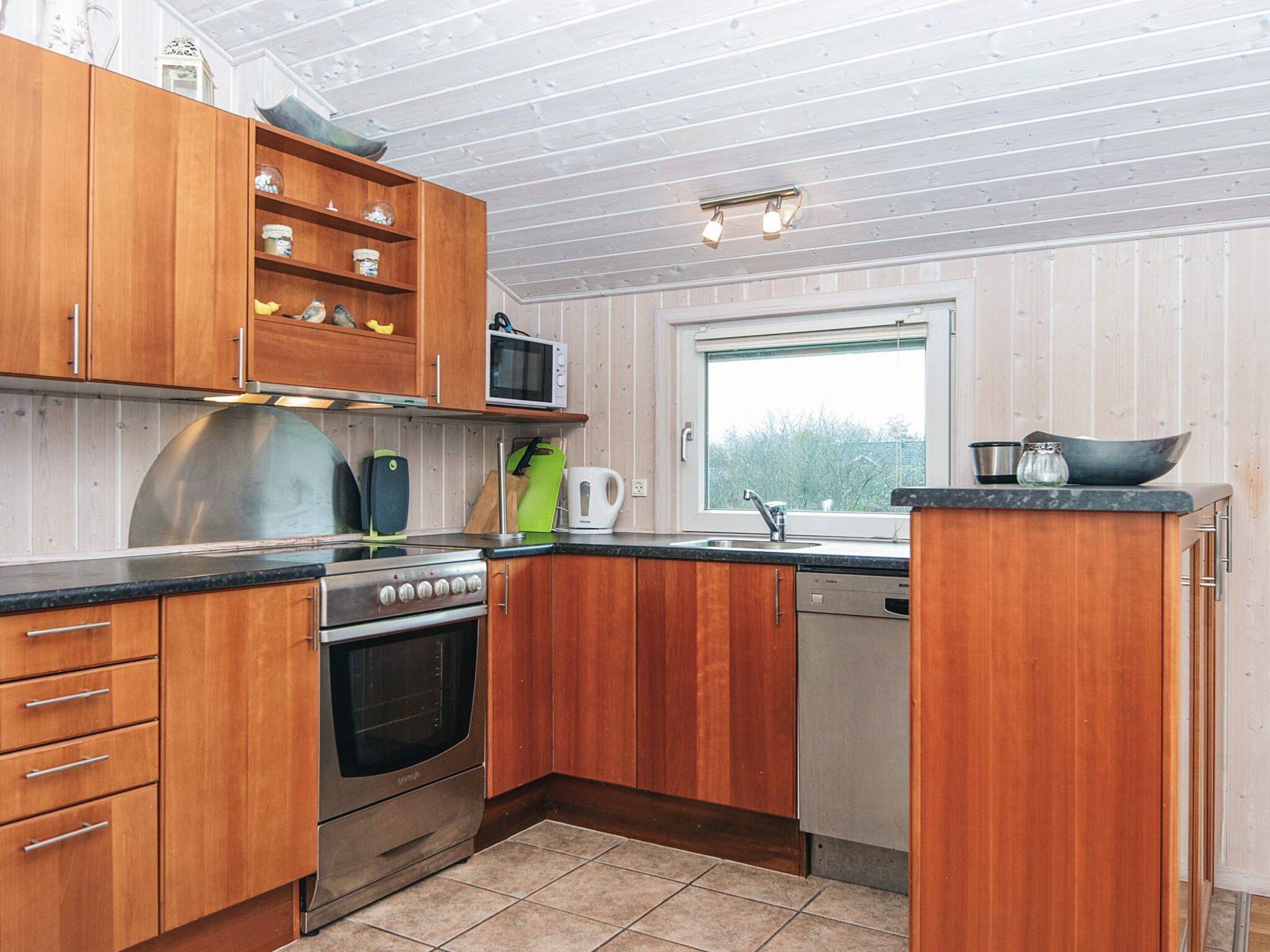 A compact kitchen with wooden cabinets, a stainless steel stove, a microwave, and a window providing natural light.