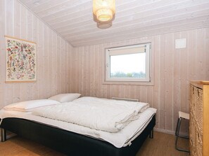 A bedroom with a bed, a window, a wall-mounted light fixture, and a framed botanical illustration.