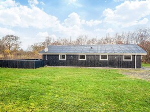A single-story wooden building with a metal roof, a fenced yard, and a clear sky.