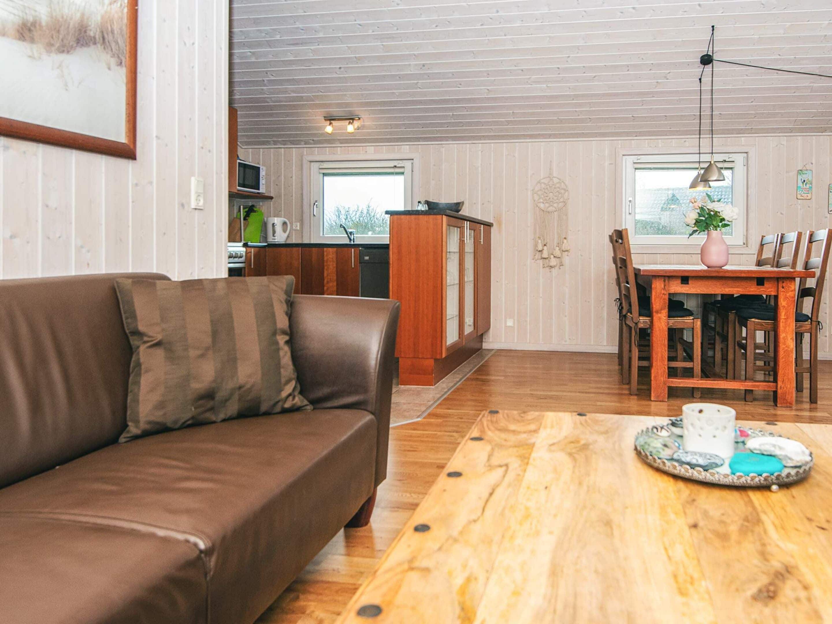 Un salon chaleureux avec un canapé en cuir marron, une table à manger en bois avec des chaises, et un coin cuisine doté de meubles en bois et d’un four à micro-ondes.