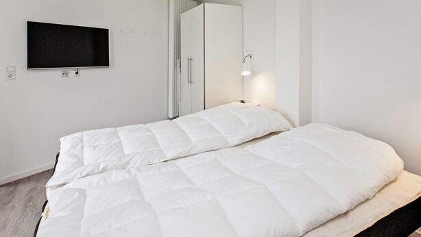 A bedroom with a bed, a wardrobe, a television, and a wall-mounted light. - Holiday Home in Wendtorf (Wendtorf)