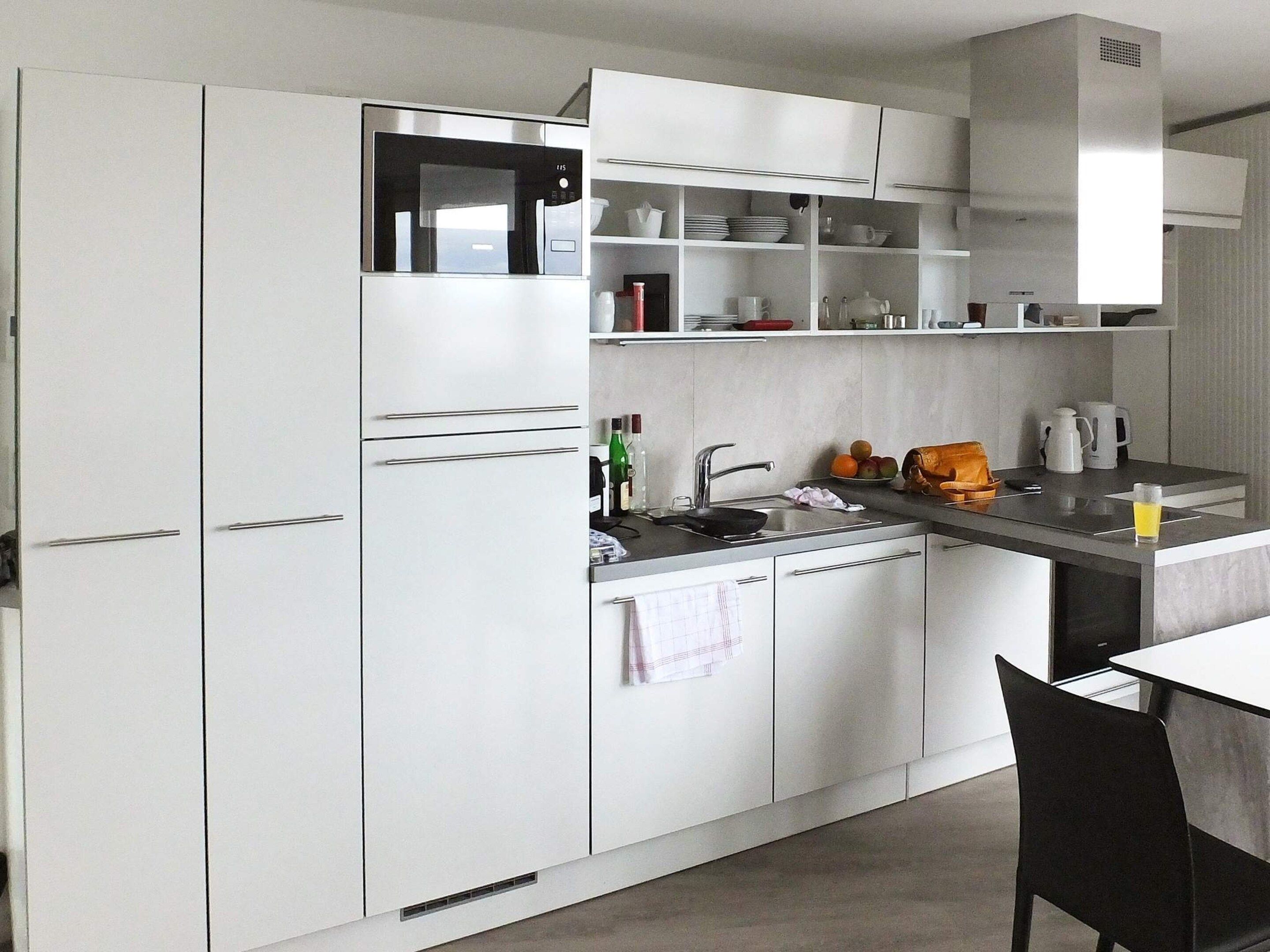 A modern kitchen with white cabinets, a built-in microwave, a sink, and a dining area with a table and chairs.