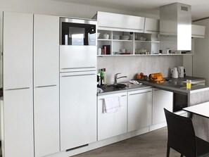 A modern kitchen with white cabinets, a built-in microwave, a sink, and a dining area with a table and chairs. - Holiday Home in Wendtorf (Wendtorf)