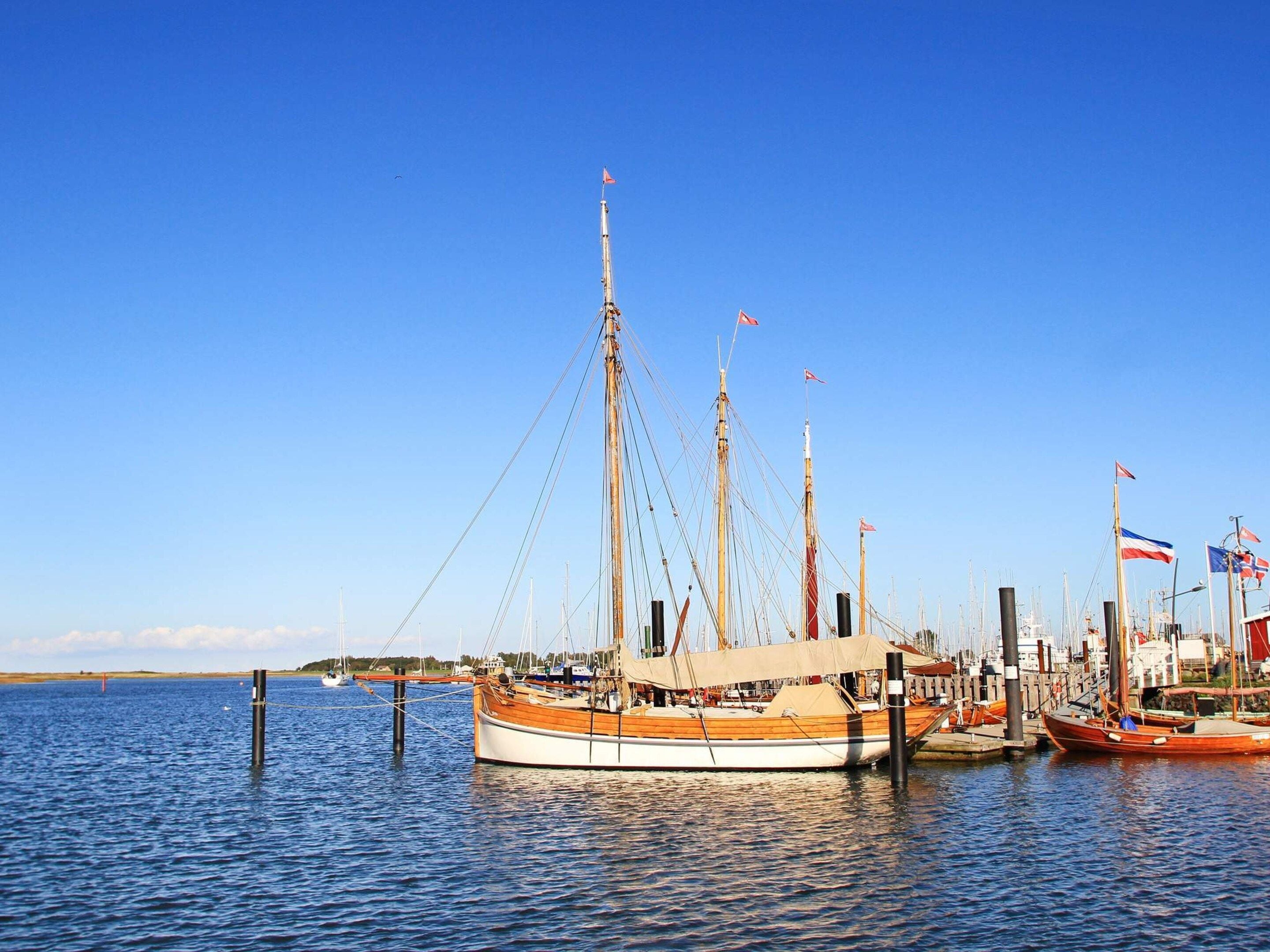 Ein Hafen mit einem großen Segelschiff, umgeben von kleineren Booten und Flaggen.
