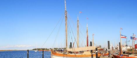 Ein Hafen mit einem großen Segelschiff, umgeben von kleineren Booten und Flaggen.