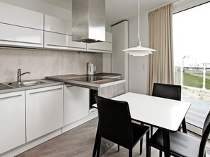 A modern kitchen with a built-in stove, a sink, and a dining area with a table and chairs. - Holiday Home in Wendtorf (Wendtorf)