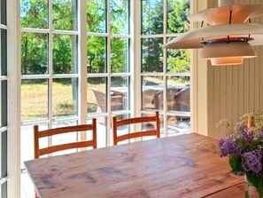 A dining area with a wooden table and chairs, large windows with a view of greenery, and a hanging light fixture.