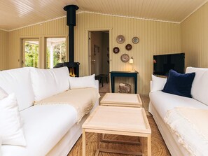Una sala de estar acogedora con dos sofás blancos, una mesa de centro de madera, una chimenea negra y un televisor.