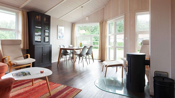 A spacious living area with a wooden ceiling, a dining table with chairs, a sofa, a glass coffee table, and a fireplace. - Holiday Home in GrÃ¶mmitz (Groemitz)