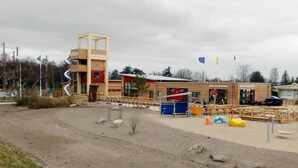 A building with a unique spiral staircase, a playground area with colorful equipment, and a sandy ground.