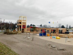 A building with a unique spiral staircase, a playground area with colorful equipment, and a sandy ground.