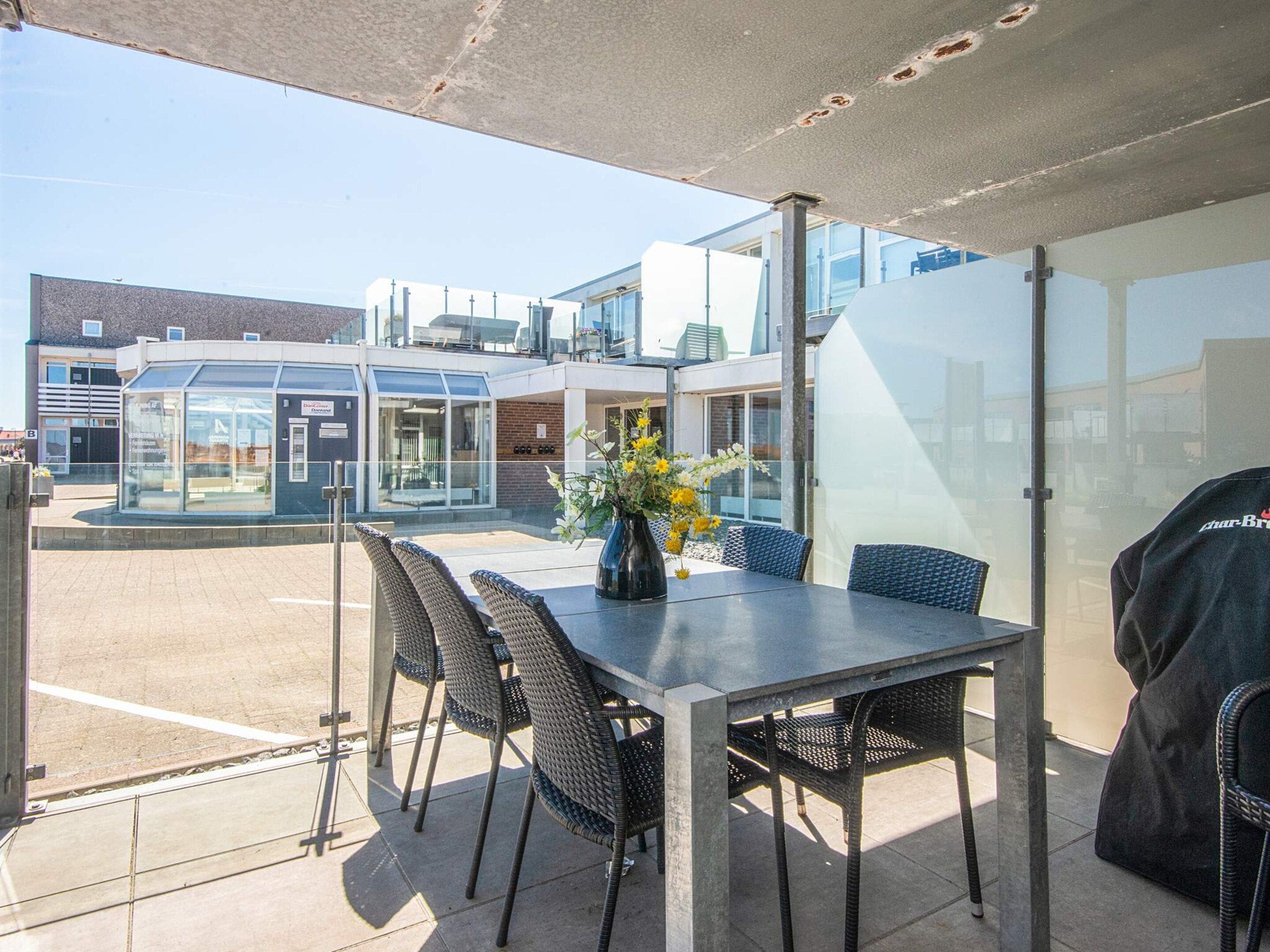 An outdoor patio area with a table and chairs, a vase with flowers, and a glass enclosure in the background.