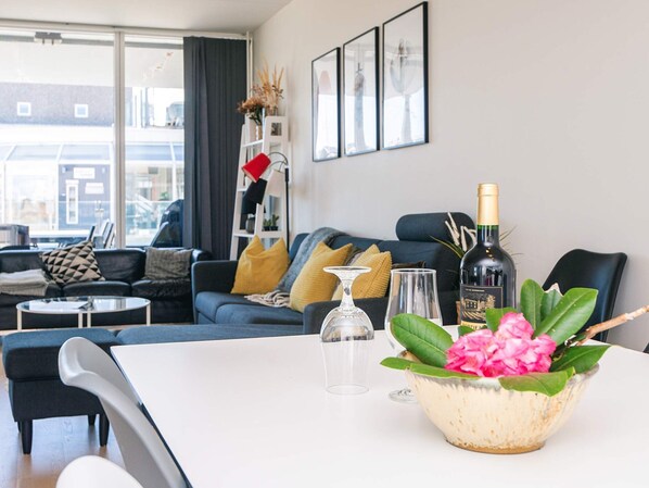A modern living room with a sofa, coffee table, and a dining table with a vase of flowers.