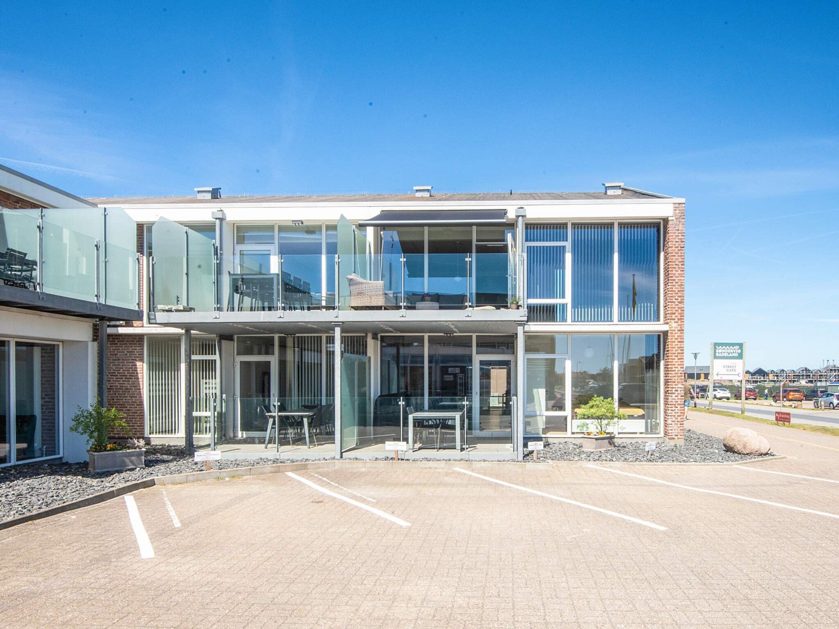 A modern building with a glass facade, a covered outdoor seating area, and a parking lot.