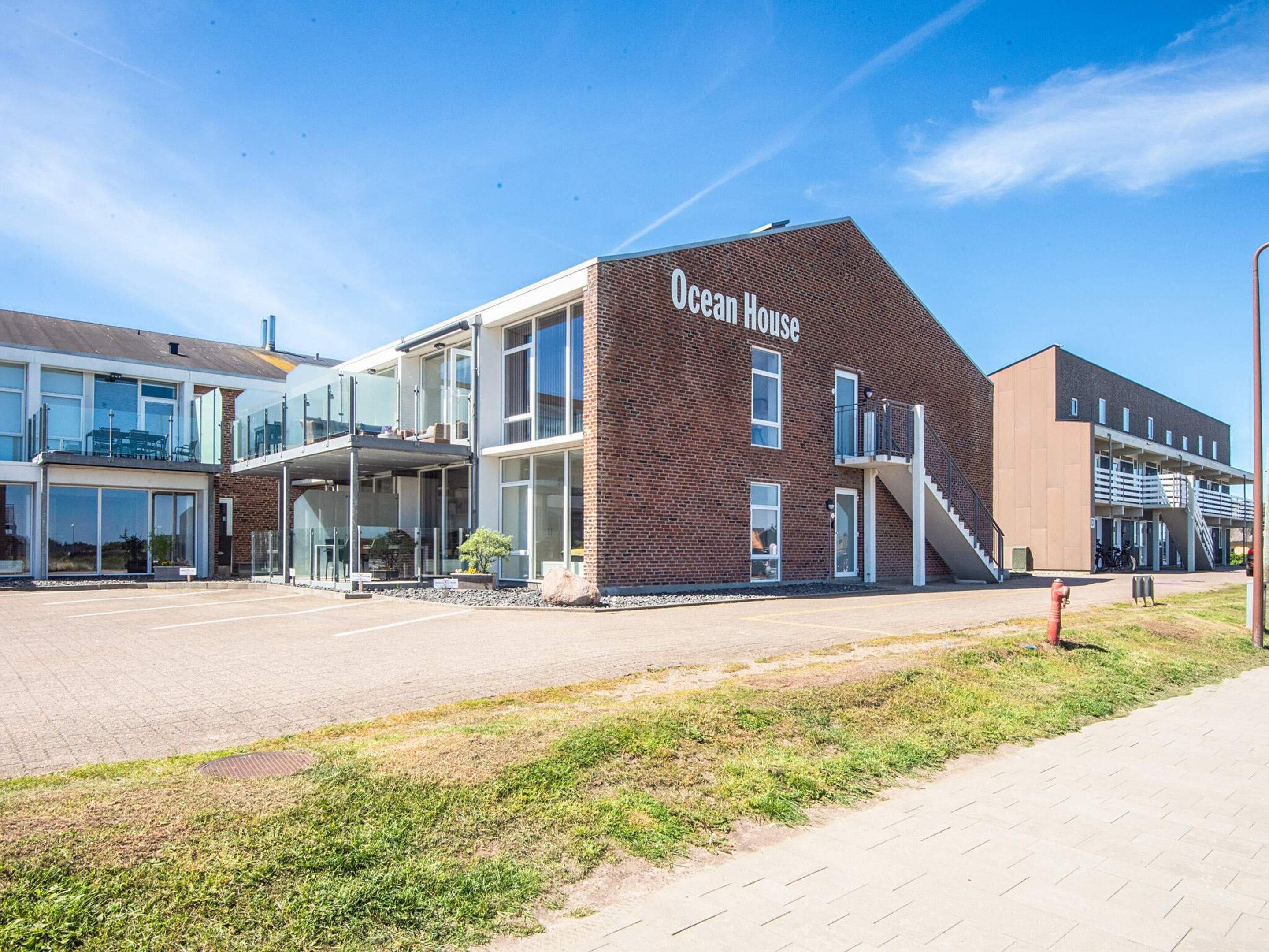 A modern building with a sign reading 'Ocean House,' featuring a brick facade, large windows, and a covered outdoor area.