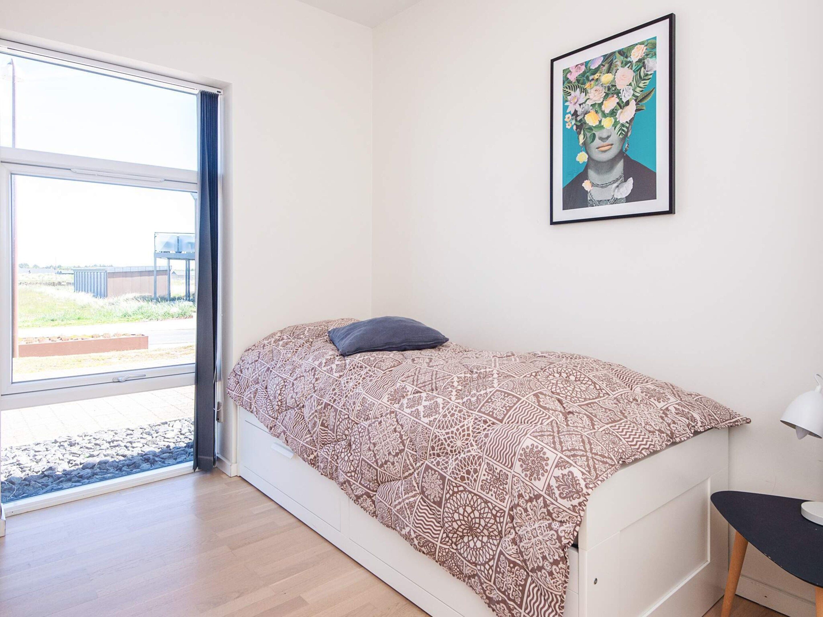 A bedroom with a bed, a window, a door, and a wall-mounted picture.