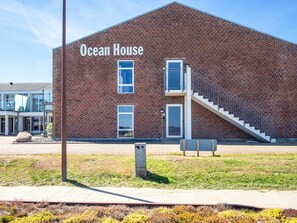 Un edificio de ladrillo con un letrero que dice 'Ocean House', una escalera y un área pavimentada con césped y arbustos.