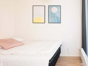 Une chambre à coucher avec un lit, une fenêtre et deux œuvres d’art encadrées accrochées au mur.