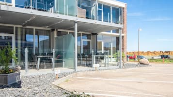 A modern building with a glass facade, outdoor seating area, and a parking lot.