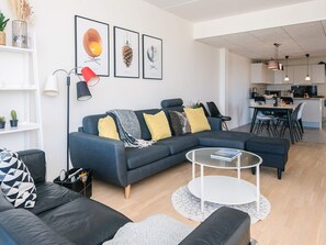 A modern living room with a sectional sofa, a coffee table, and a dining area with a kitchen in the background.
