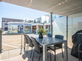 An outdoor patio with a table and chairs, a vase with flowers, and a grill.