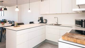A modern kitchen with white cabinetry, a central island, a sink, and a microwave.