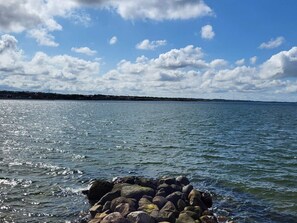 A calm body of water with a rocky shoreline and a distant view of wind turbines. - 5 Star Holiday Home in Vinderup (Vinderup)
