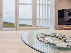 A modern interior with a large window overlooking a body of water, a wooden floor, and a glass table with decorative stones. - 5 Star Holiday Home in Vinderup (Vinderup)