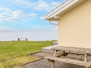 Una mesa de picnic y un banco junto a una propiedad frente al agua, con vista al mar.
