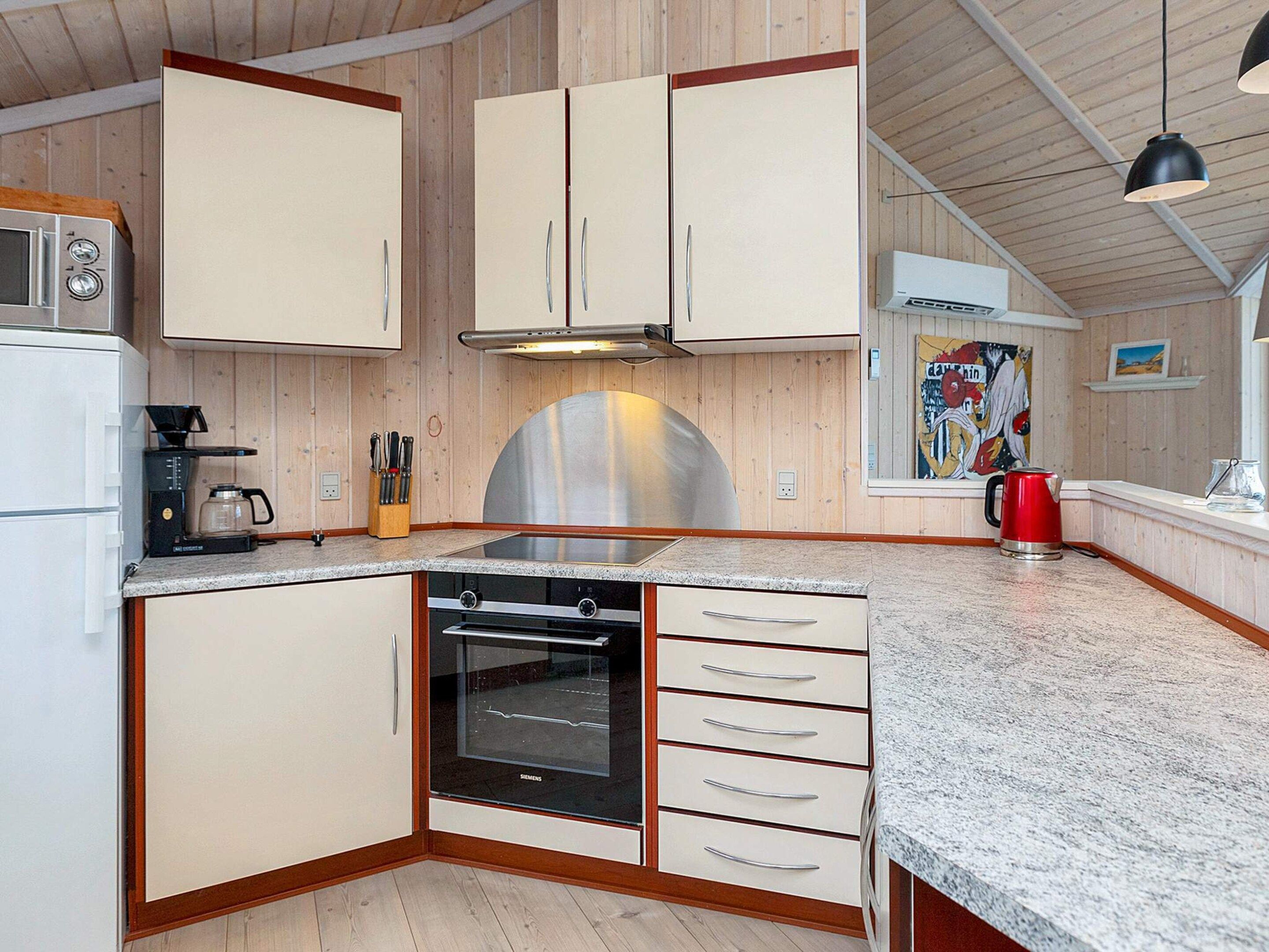 A kitchen with wooden cabinets, a stainless steel range hood, a coffee maker, and a red kettle.